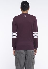 Maglione a maglia color bordeaux con dettagli a strisce bianche sulle maniche. Presenta un piccolo logo sulla parte posteriore del collo e polsini a costine. Tessuto morbido e vestibilità informale.