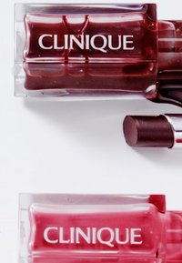 To produkter fra Clinique i klare plastbeholdere. Den ene er dyp rød, den andre er en lysere rosa. Begge har hvit merking på forsiden.