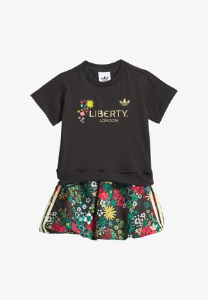 Musta lyhythihainen paita, jossa on kullanvärinen "LIBERTY. LONDON" -teksti, yhdistetty värikkääseen kukkamekkoon, jossa on vihreitä, punaisia ja keltaisia kuvioita.