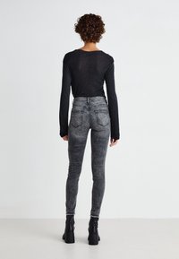 Camisa negra de manga larga combinada con jeans ajustados grises de cintura alta. Los jeans presentan un desgaste descolorido y bolsillos traseros, acompañados de botas negras hasta el tobillo.