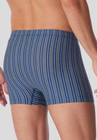 Námorně modré plavkové šortky se širokými pruhy v zelené a bílé barvě, mají těsný střih a elastický pás.