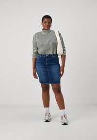 Blusa de gola alta listrada em preto e branco, combinada com uma saia de ganga azul até ao joelho. Acessórios incluem uma mala de ombro em creme claro e ténis.