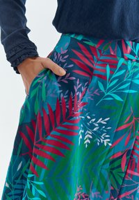 Falda floral en patrones vibrantes de verde, rojo y azul; cuenta con un tejido suave y liviano y un bolsillo lateral.