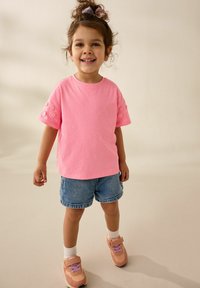 Roze katoenen t-shirt met korte mouwen, versierd met bloemenborduursels, gecombineerd met denim shorts en rozen sneakers met paarse accenten.