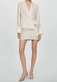 Růžová zavinovací blůza s dlouhými rukávy, bílými manžetami a bočním zavazováním. V kombinaci s světle šedou mini sukní a stříbrnými sandály na podpatku.