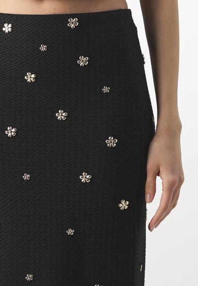 Jupe noire texturée avec un motif en zigzag et des appliqués floraux argentés éparpillés, présentant une silhouette ajustée.