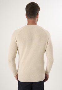 Beige Ribbenstrickpullover mit langen Ärmeln und Rundhalsausschnitt. Bietet eine subtile Textur und eine figurnahe Form, ideal für legere Anlässe.