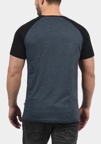 Muška majica s tamnoplavim tijelom i crnim raglan rukavima. Kratki rukavi, okrugli izrez i glatka tekstura.