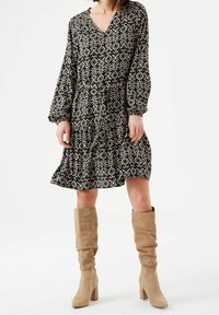 Svart och vit mönstrad klänning med långa ärmar, V-ringning, cinchad midja och utsvängd kjol, tillsammans med knähöga beiga mockastövlar.