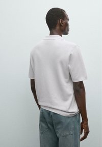Polo shirt grigio chiaro a maniche corte con colletto dritto, realizzato in tessuto morbido, abbinato a jeans di denim blu sbiaditi.