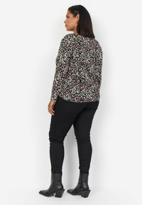 Haut noir à manches longues avec un motif léopard multicolore, associé à un pantalon skinny noir et des bottines à talons noires.