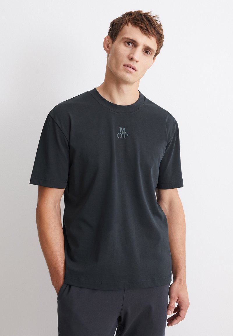 Svart kortärmad t-shirt i mjuk bomull med rund halsringning, försedd med en liten blå logotyp (MOP) centrerad på bröstet.