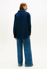 Diepblauw oversized shirt van zachte stof, met een platte kraag en afgeronde onderkant, gecombineerd met losse, high-waisted lichtblauwe jeans.