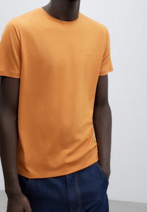 T-shirt en coton orange avec un col rond, des manches courtes et une texture lisse. Présente un logo de marque subtil cousu sur la poitrine.