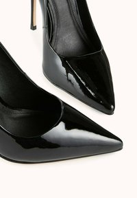 Chaussures à talons aiguilles en cuir verni noir avec un bout pointu et une texture lisse ; elles présentent un design épuré et un talon stiletto fin.