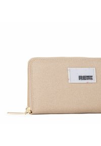 Beige stofpung med en tekstureret overflade, guld lynlås og et hvidt mærke med teksten "RENEW VITA." Kompakt rektangulær form.