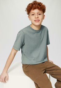 Lichtgroene katoen t-shirt met korte mouwen, ronde hals en een ontspannen fit, gedragen met bruine broek. Eenvoudig ontwerp, gladde textuur.