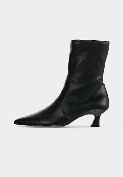 Botte mi-mollet en cuir noir avec bout pointu et petit talon kitten, vue de profil sur un fond clair uni.