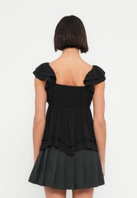 Μαύρο φόρεμα με ραμπούλες στα τιράντες, κορσάζ με σφηκοφωλιά και φούστα με στρώσεις και διακριτική υφή. Η φούστα είναι πιο σκούρα στο κάτω μέρος.