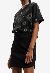 Svart t-shirt med cirkulära silverdetaljer, kombinerad med en svart minikjol och en texturerad spännbälte, med en stilren design.