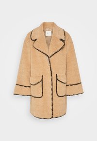 Beżowy płaszcz teddy z czarną lamówką, oversize, z klapowanym kołnierzem, szerokimi rękawami i dwoma przednimi kieszeniami. Miękka, teksturowana tkanina na całej powierzchni.