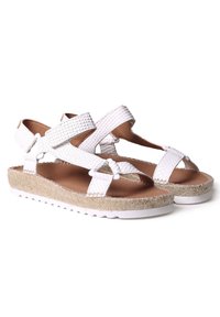 White woven sandals with cross straps, featuring an espadrille jute sole and a textured finish. Soft brown insole with white rubber outsole.