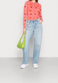 Maglietta rosa chiaro a maniche lunghe con motivi di frutta, colletto con bottoni; abbinata a jeans a gamba larga blu chiaro. Porta una piccola borsa verde.