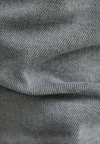 Tela de mezclilla gris con una superficie suave y texturizada, que presenta un patrón de espiga y un ligero estiramiento, doblada para dar profundidad visual.