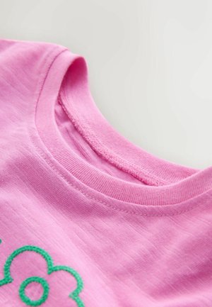 Różowy bawełniany t-shirt z zaokrąglonym dekoltem i widocznym, fakturowanym przeszyciem. Na froncie znajduje się zielony haftowany wzór kwiatu.