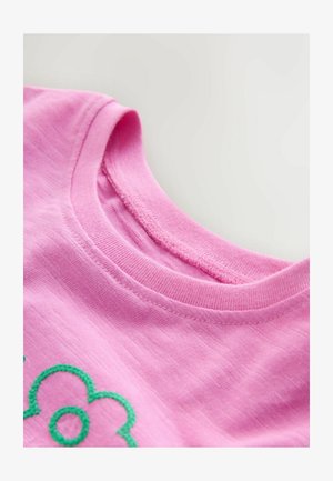 Roosa puuvillane T-särk ümarate kaelusega ja nähtavate tekstuursete õmblustega. Esiküljel on roheline tikitud lillemuster.