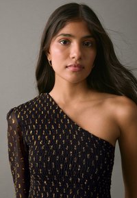 Abito in tessuto nero testurizzato con dettagli dorati, design monospalla, manica lunga trasparente e dettagli plissettati sul corpetto.