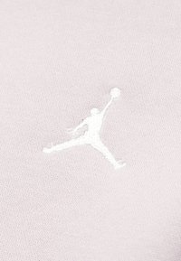 Κεντημένο λευκό περίγραμμα ενός παίκτη μπάσκετ που πηδάει με την μπάλα σε ανοιχτό μωβ πλεκτό ύφασμα.