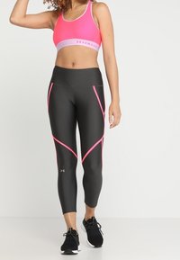 Leggings de sport noirs avec des accents géométriques roses, assortis à un soutien-gorge de sport rose vif avec une bande violet clair, conçus pour le fitness.