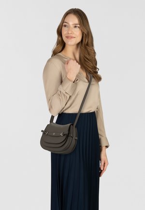 Borsa a tracolla in pelle grigio scuro, caratterizzata da un design curvo, patte sovrapposte e ferrature argentate. Abbinata a una blusa beige e una gonna plissettata blu navy.