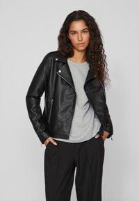 Black leather asymmetrical motorcycle jacket with silver hardware, zip pockets, and a smooth texture, layered over a gray shirt.