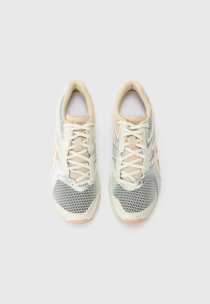 Zapatillas deportivas ligeras con parte superior de malla en crema y gris, con acentos texturizados y suela acolchada beige.