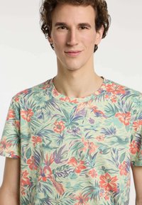 T-shirt met korte mouwen van lichte stof, met een multi-kleurig bloemenpatroon in groene, rode en paarse tinten. Ronde halslijn.