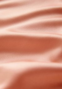 Zacht, perzikkleurig stof met een gladde textuur, met zachte golven en een subtiele glans. Ideaal voor kledingstukken of zachte bekleding.