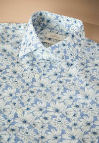 Modrá kvetinová košeľa na zapínanie na gombíky s bielymi a tmavomodrými kvetmi, vybavená špicatým golierom a tromi viditeľnými bielymi gombíkmi.