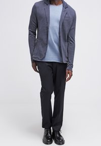 Herrgrå stickad kavaj med notched slag, kombinerad med en ljusblå tröja med rund hals och svarta byxor. Svarta dressade skor fulländar looken.