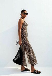 Robe imprimée léopard avec une silhouette ajustée, fentes sur les côtés, associée à des sandales à glissière noires et un sac fourre-tout en maille noire sur fond blanc.