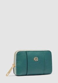 Portefeuille en cuir bleu sarcelle à fermeture éclair tout autour avec une fermeture éclair dorée et un petit logo doré sur le devant, présenté sur un fond gris clair uni.