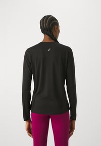 Long-sleeved black athletic top, smooth fabric, round neckline, features a small logo at the back, complemented by bright pink pants.