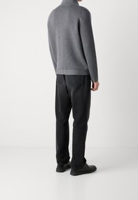 Šedý pletený svetr s vysokým límcem, doplněný černými džínovými kalhotami. Oblečení má volný střih a minimalistický design.