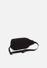 Sac banane noir en tissu doux, de forme rectangulaire, avec fermeture éclair et sangle ajustable pour un port sécurisé.