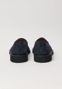 Zapatos de ante azul marino con suela de goma negra plana, con puntera redondeada y una silueta simple; textura suave sin acentos visibles.