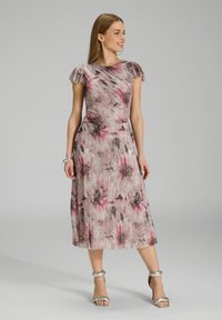 Robe à imprimé floral dans des tons de rose doux, gris et crème. Texture plissée, manches courtes volantes et longueur sous le genou. Associée à des talons argentés.