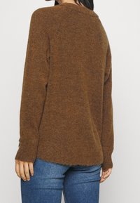 Suéter marrón de textura suave con mangas largas y un corte relajado. Presenta un dobladillo ligeramente curvado y puños acanalados.