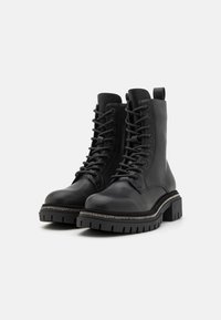 Black leather combat boots with a thick sole, lace-up design, reinforced toe, and decorative metallic trim along the edge.