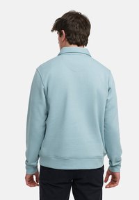 Ljusblå sweatshirt med krage, långa ärmar och ribbade manschetter. Tyget verkar mjukt och något texturerat.